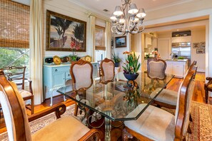 Uma sala de jantar com mesa de vidro, cadeiras de madeira e um candelabro.