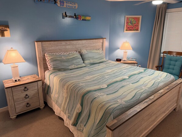 A bedroom with a bed, two bedside tables, a nightstand, a lamp, a clock, and a window with curtains. - Beautiful 2 Bedroom Condo in Ocean Creek Resort (Myrtle Beach)