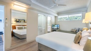 Ein modernes Hotelzimmer mit einem großen Bett, einem Schreibtisch mit Computer, einem Badezimmer und Blick ins Freie.