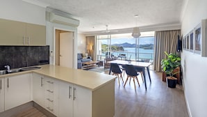 Eine moderne Küche mit einer großen Kochinsel, ein Essbereich mit Ausblick und ein Wohnbereich mit Balkon, der auf eine reizvolle Landschaft blickt.