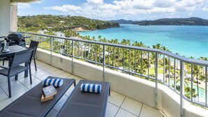 Ein Balkon mit Meerblick, einem Tisch mit Stühlen und einer Lounge-Ecke mit gestreiftem Kissen.