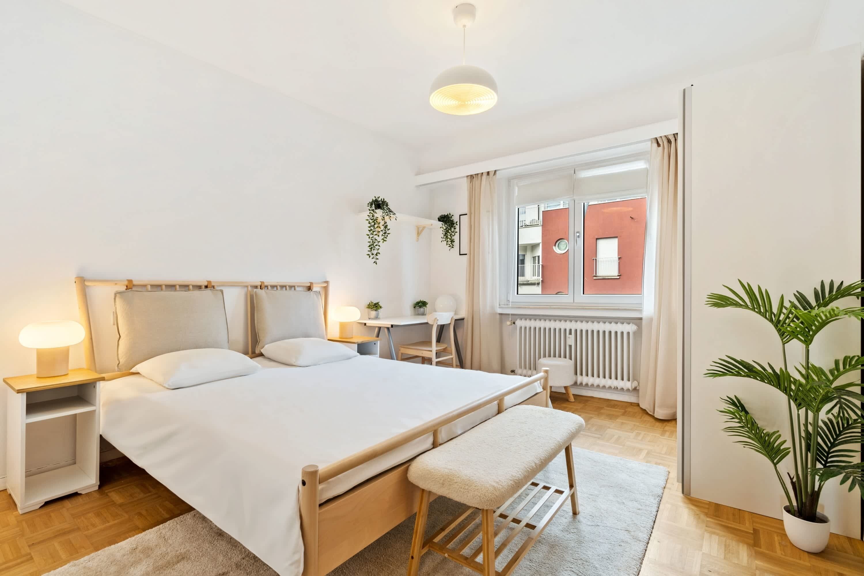Een moderne slaapkamer met een houten bed, nachtkastjes, een bureau en een potplant.