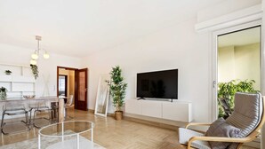 Un soggiorno moderno con televisore, zona pranzo e angolo salotto con una poltrona e un tavolino.