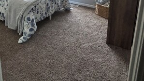 Un dormitorio con cama, ventilador de techo, ventana con persianas y un pequeño armario de madera.
