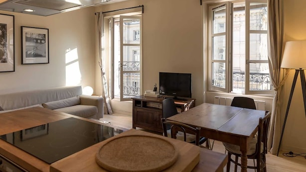 A modern living room with a sofa, a dining table with chairs, a TV, and a kitchen area with a stove. - Rivoli Market I Comfortable 1 Bed Apt near Hotel de Ville (Paris)
