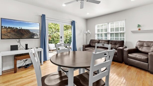 A modern living room with a round dining table, white chairs, a brown leather sofa, and a television mounted on the wall.