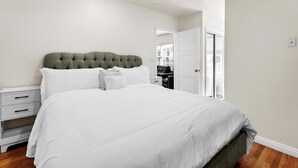 A bedroom with a tufted headboard, white bedding, a nightstand, and a wooden floor.
