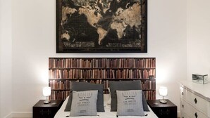A bedroom with a large world map on the wall, a bookshelf filled with books, a bed with two pillows, and a dresser with drawers. - Stylish Sevre I Chic 1-BR in the Heart of the 6th (Paris)