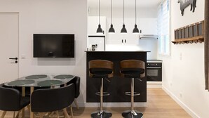 A modern kitchen with a central island, black bar stools, a flat-screen TV, and pendant lighting. - Stylish Sevre I Chic 1-BR in the Heart of the 6th (Paris)