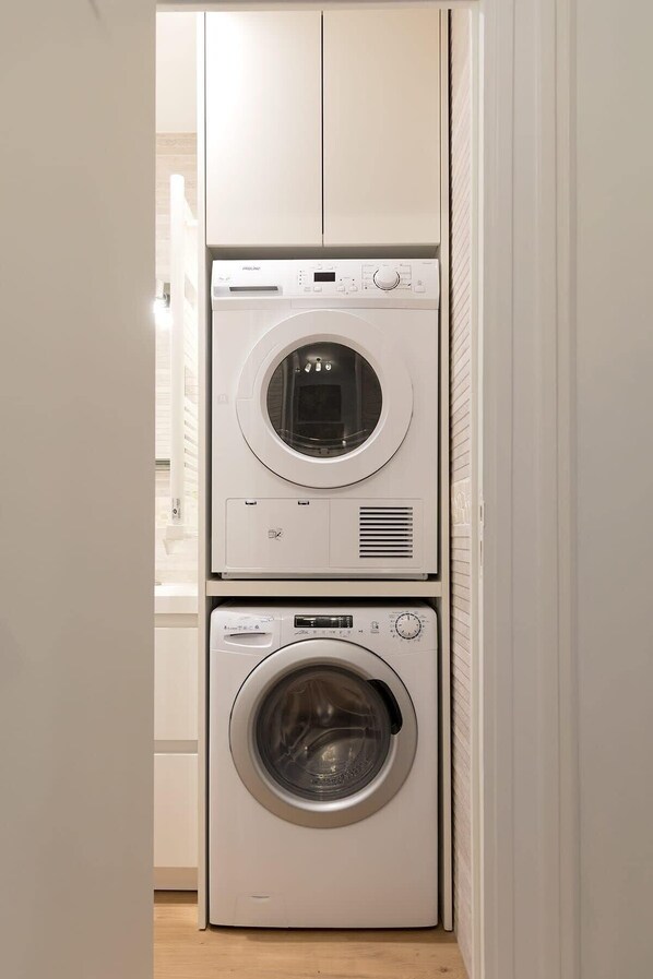 Une buanderie équipée de deux machines à laver superposées, d’un sèche-linge et d’un meuble de rangement.