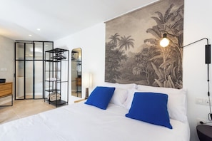 Un dormitorio con cama, dos almohadas azules, una lámpara de pared y un mural tropical.