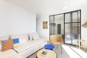 Una sala de estar moderna con un sofá, una silla de mimbre, una mesa de centro redonda y un puerta corrediza de vidrio.
