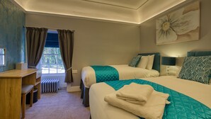 Habitación de hotel con dos camas, un escritorio y una ventana con cortinas.
