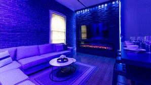 Ein modernes Wohnzimmer mit Backsteinwand, einer Couch, einem Couchtisch, einem Kamin und einem Essbereich mit gedecktem Tisch.