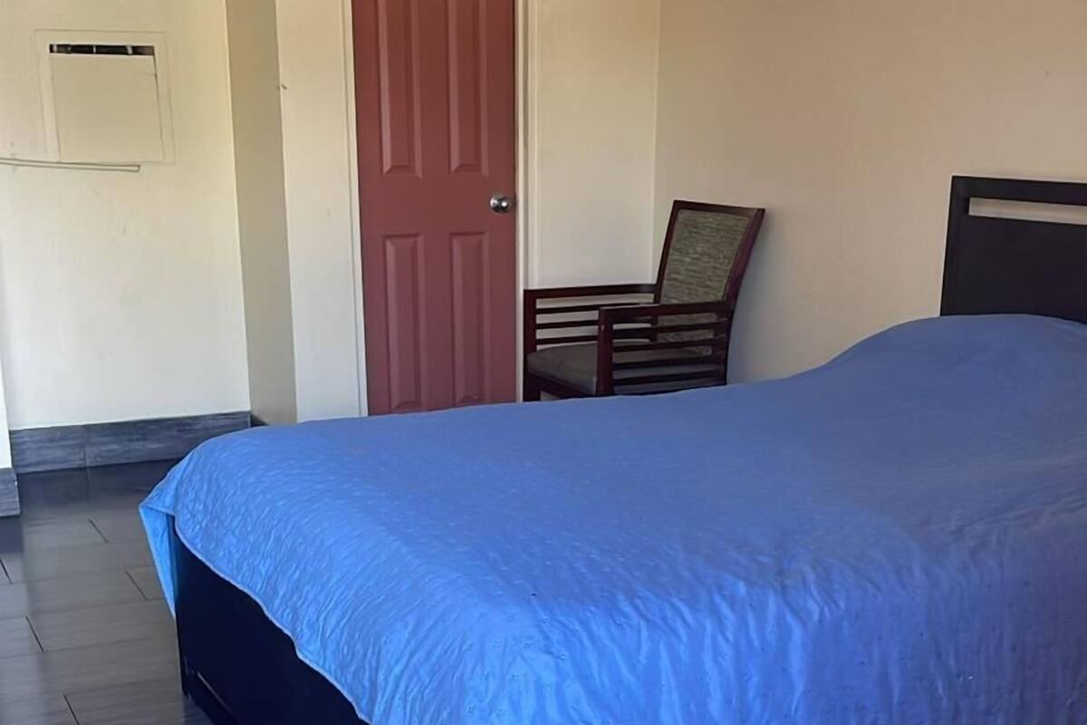 Um quarto com cama, uma cadeira, uma porta e um ar-condicionado fixado na parede.
