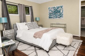 A bedroom with a bed, bedside tables, a lamp, a rug, and a painting on the wall.
