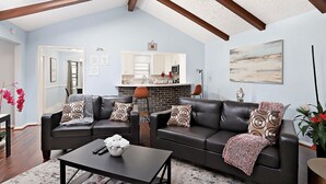 A living room with a dark leather sofa, a coffee table with a vase, and a kitchen in the background. - Family Ready Spacious Retreat - 4BR, Sleeps 8, Pet Friendly with Gazebo (Houston)