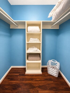 A closet with shelves holding folded towels, a laundry basket, and a wooden floor.