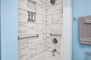 Une salle de bain avec une douche, des carreaux de marbre, un porte-serviettes et un sĂšche-mains.