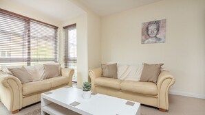 Ein Wohnzimmer mit zwei beigefarbenen Sofas, einem weißen Couchtisch und einem Buddha-Gemälde an der Wand.