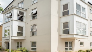 Ein mehrstöckiges Wohngebäude mit schlichter Fassade, großen Fenstern und einem Balkon im Erdgeschoss.