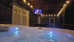 Ein Bereich mit Whirlpool, Fernseher, Steinwänden und Lichterkette.