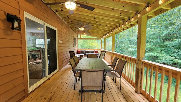 Eine Holzterrasse mit Tisch und Stühlen, eine Schiebetür und Blick auf einen Wald.