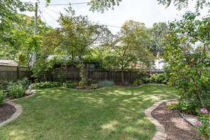 A well-maintained backyard with a lawn, trees, and a wooden fence. - Firefly Cottage - close to beach & town! (South Haven)