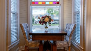 A dining area with a table and two chairs, a stained glass window above, and a view of a residential street.