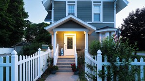 A two-story house with a front porch, a white picket fence, and a pathway leading to the entrance.