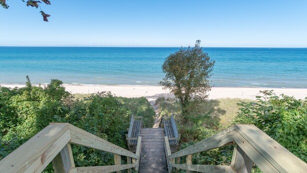A wooden staircase leading to a beach with clear blue water and a sandy shore. - Haven Hideaway by Cottages on Wash is the perfect vacation home! (South Haven)