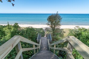 A wooden staircase leading to a beach with clear blue water and a sandy shore. - Haven Hideaway by Cottages on Wash is the perfect vacation home! (South Haven)