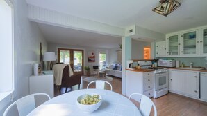 A spacious kitchen with white cabinetry, a dining area with a round table, and a living room with a sofa and a painting. - Haven Hideaway by Cottages on Wash is the perfect vacation home! (South Haven)