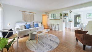 A living room with a sofa, ottoman, coffee table, and a round rug. There is a kitchen area visible through an open doorway. - Haven Hideaway by Cottages on Wash is the perfect vacation home! (South Haven)