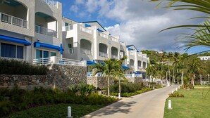 A row of white buildings with blue accents, a stone wall, and a paved walkway with palm trees. - Very Romantic Secluded Beach Getaway in St. Thomas Island (St. Thomas)