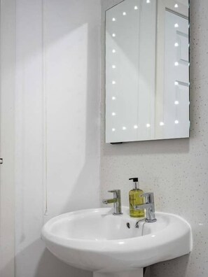 Een badkamer met een witte wastafel, een spiegel met verlichting en een zeepdispenser.
