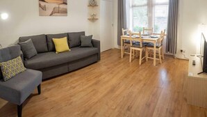 A living room with a grey sofa, a dining table with chairs, a painting on the wall, and a large window with curtains. - ☆ Quiet Ground Floor Apartment Near University ☆ (Dundee)