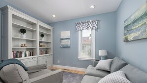 Uma sala de estar com um sofá cinzento, uma estante de livros e um quadro na parede.