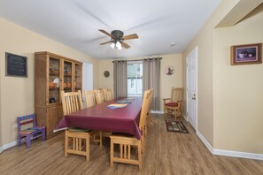 Un coin repas comprenant une table en bois, des chaises, un ventilateur de plafond, un meuble en bois et une fenêtre avec des rideaux.