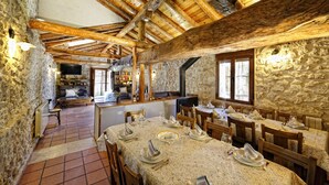 A rustic dining area with stone walls, wooden beams, and a long table set for a meal. - El Pajar de Justa (Adrados)