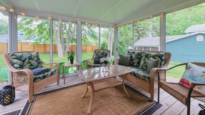 A covered patio with wicker furniture, a glass coffee table, and a view of the backyard.