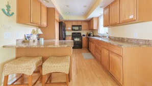 A kitchen with wooden cabinets, a granite countertop, and a built-in microwave. There are two woven stools at the island.