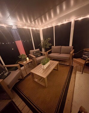 Un espace extérieur aménagé avec un canapé, des fauteuils, une table basse et une petite table sur laquelle est posée une bougie.