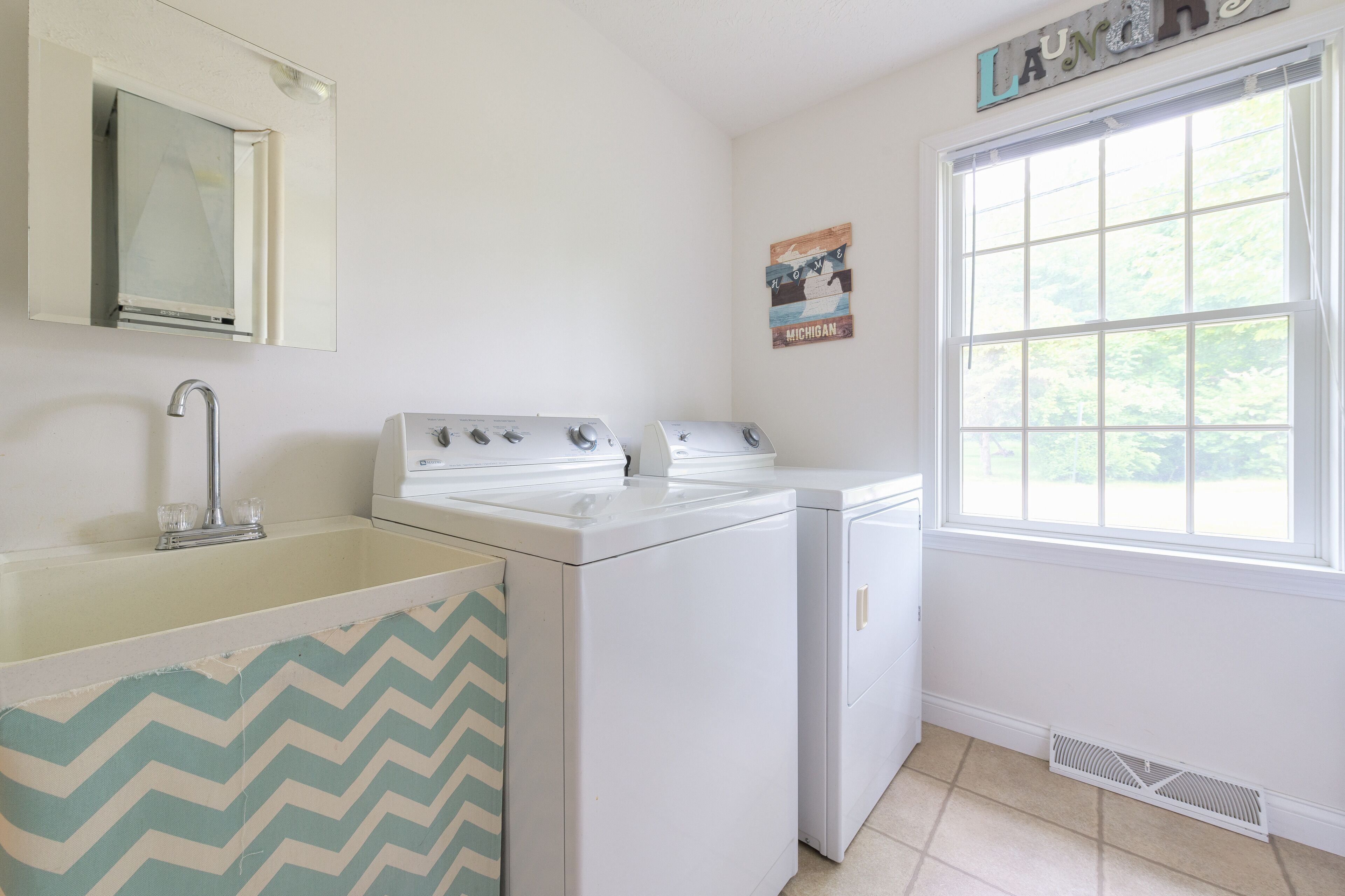 A laundry room with a sink, two dryers, a window, and a mirror.