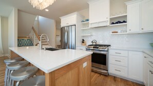 A modern kitchen with white cabinetry, stainless steel appliances, and a central island with bar stools. - Beach Breeze - 5 bedroom 4.5 bath vacation rental located just a block from the beach! (South Haven)