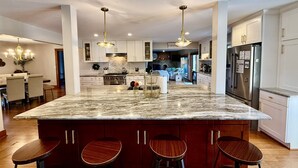 Una cocina moderna con una isla grande, taburetes de bar y un comedor con candelabro.