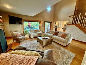 A spacious living room with a large sofa set, a coffee table, and a fireplace. There is a view of a patio with outdoor furniture. - Ultimate Retreat | Pool, Spa & 10 Acres (Fairport)