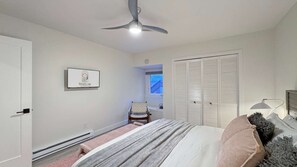 A bedroom with a bed, a ceiling fan, a window, a wardrobe, and a sign on the wall.