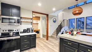 A modern kitchen with black cabinets, stainless steel appliances, and a wooden floor.