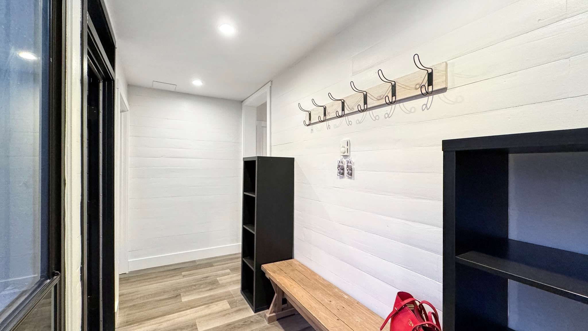 A hallway with a bench, a coat rack, and a wall-mounted shelf.